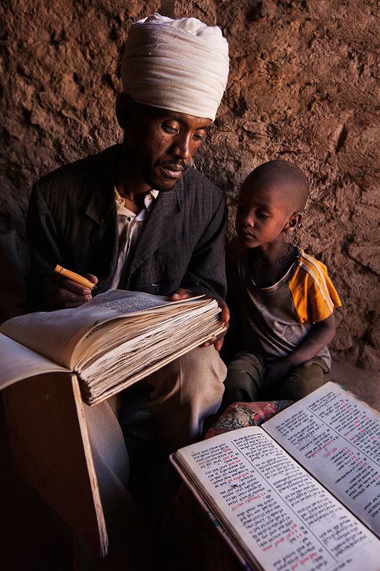 Ethiopian Orthodox priest writing text from the bible on a book made from goat…